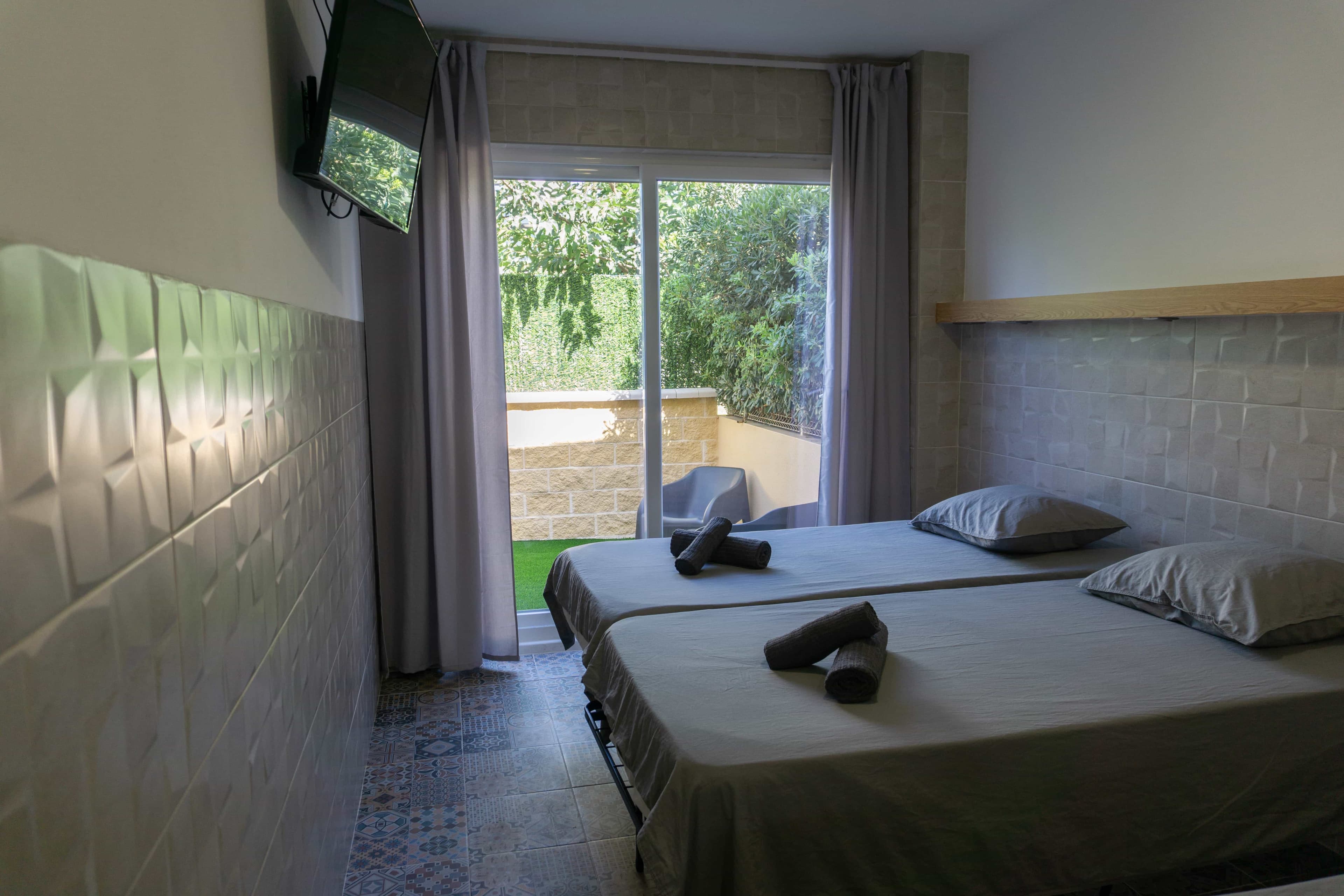 Twin beds at La Ruta, with a wall-mounted TV and the balcony door open to the garden